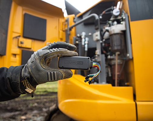 Heavy equipment technician holding up the Tekamo HD device for fleet tracking which is about to be installed in an excavator